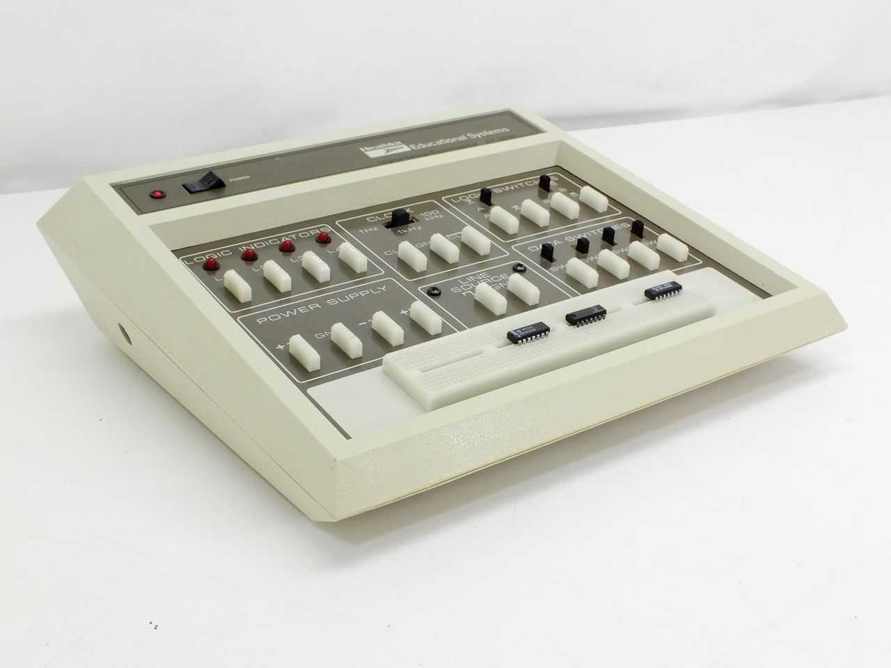 Figure 5 — The same grey unit from the front left: dark nameplate strip with LED pilot and rocker switch, the panel, and three ICs left in the breadboard.
